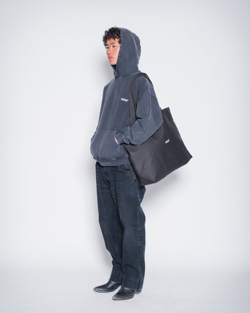 Model wearing recycled oversize black tote bag with Ikono embroidery and Ikono oversize vintage black hoodie. 