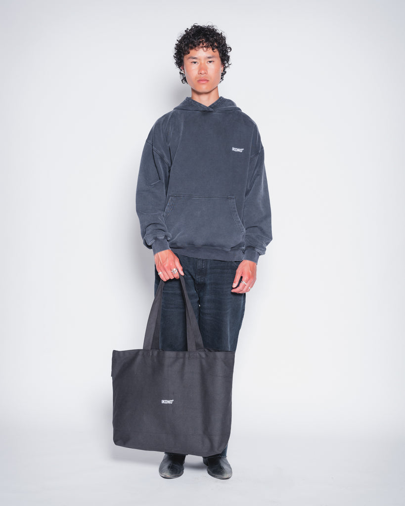 Model wearing recycled oversize black tote bag with Ikono embroidery and Ikono oversize vintage black hoodie. 