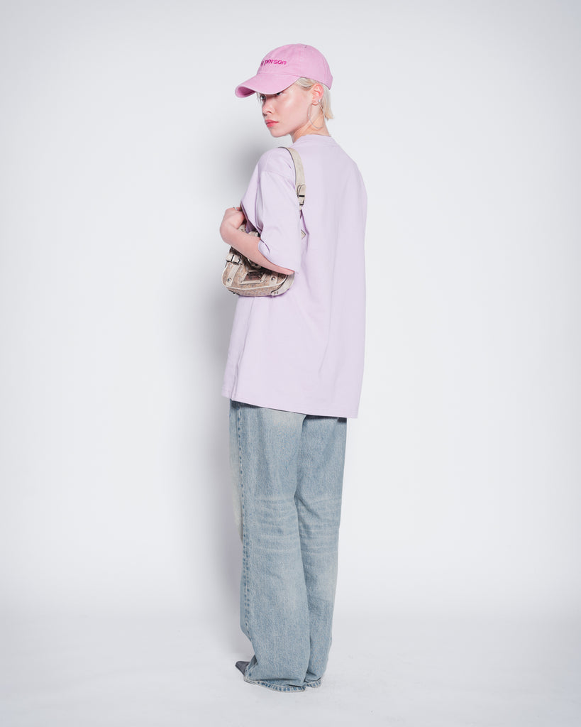 Model wearing washed pink dad cap with party person embroidery and lilac oversize t-shirt with party person print. Picture from back. 